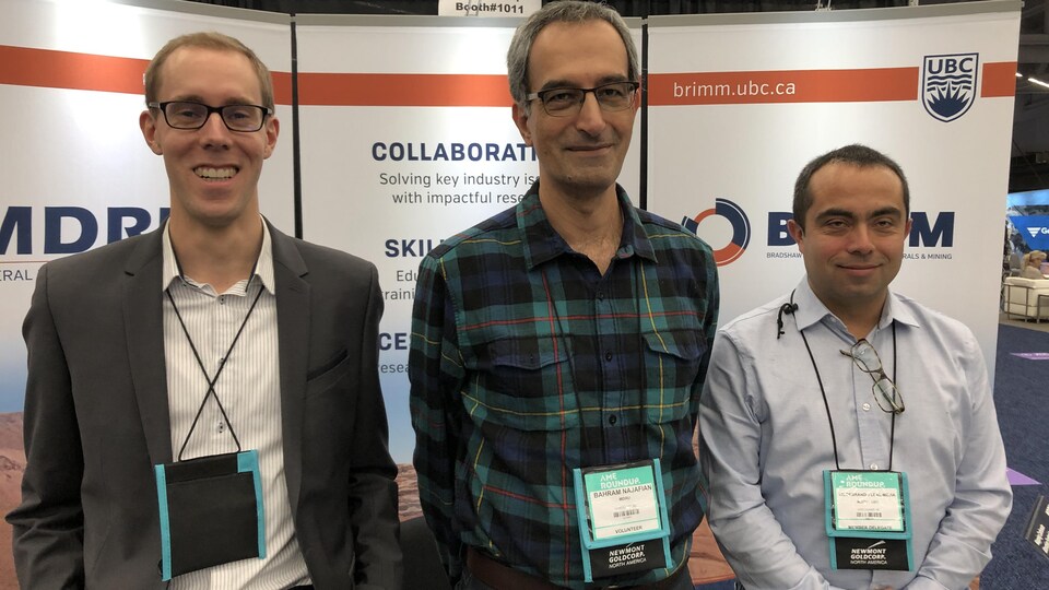 3 scientifiques posants devant un stand d'exposition.