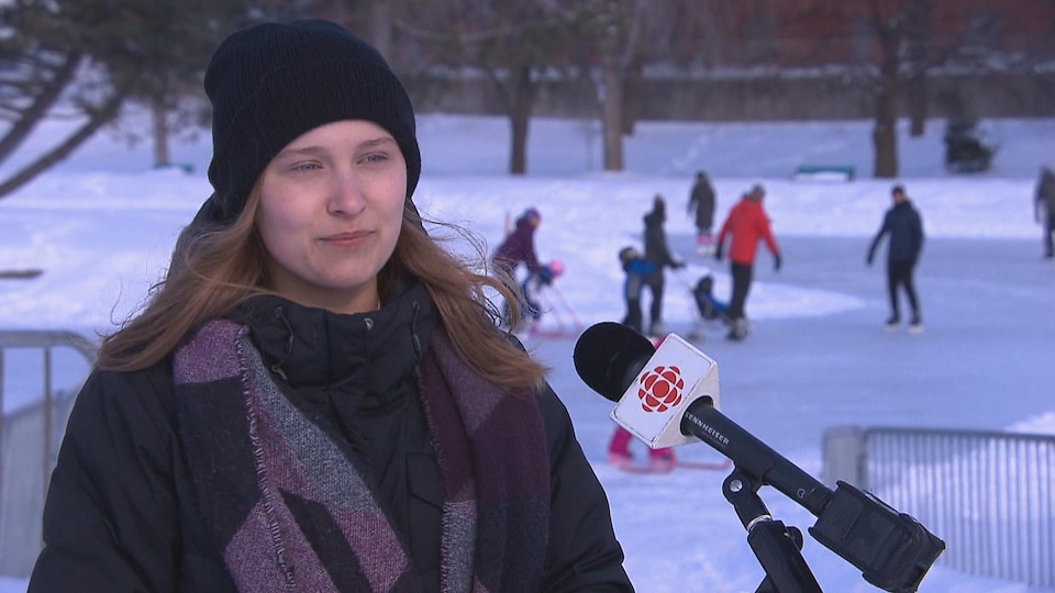 Une jeune femme vêtue d'un manteau et d'une tuque en entrevue à Radio-Canada devant un rond de glace.