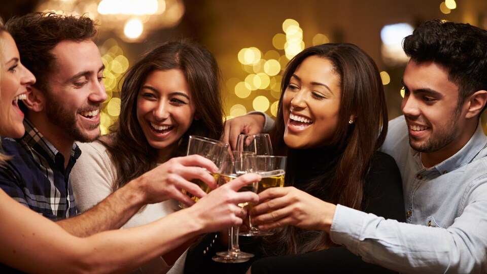 Cinq jeunes adultes trinquent en souriant.