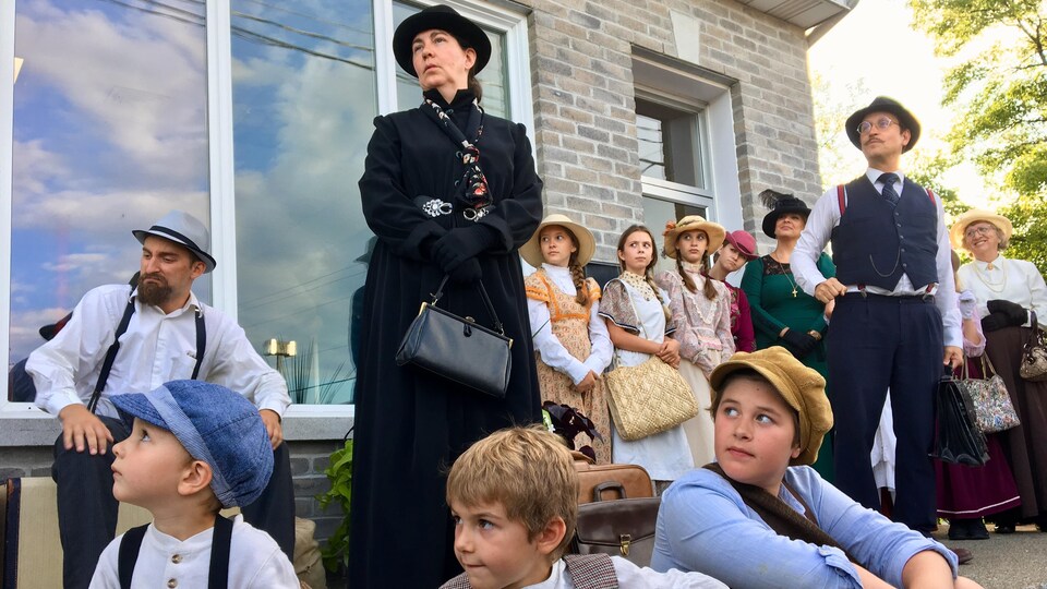 Hommes, femmes et enfants en costume d'époque participent à une pièce de théâtre extérieure.