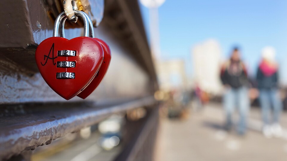 Deux cadenas rouge vif, en forme de cœur, attachés à un pont.