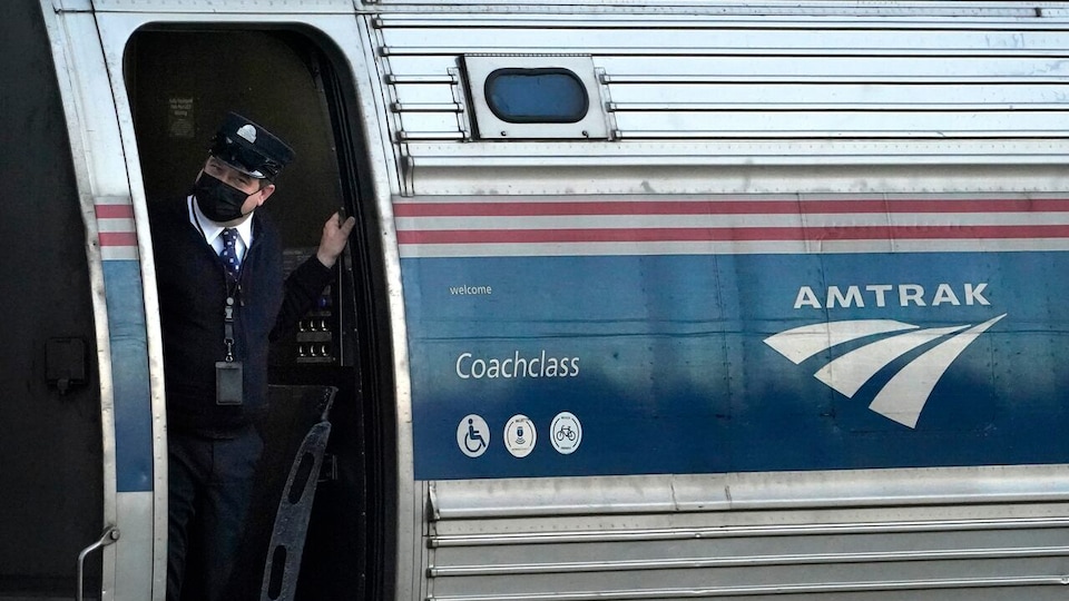 Un conducteur de train est debout devant la porte d'un wagon d'Amtrak avant qu'il ne quitte la gare de Freeport, dans le Maine.