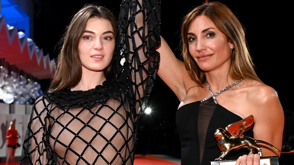Une femme lève le bras d'une autre femme sur scène en signe de victoire. Elle tient un trophée dans son autre main.