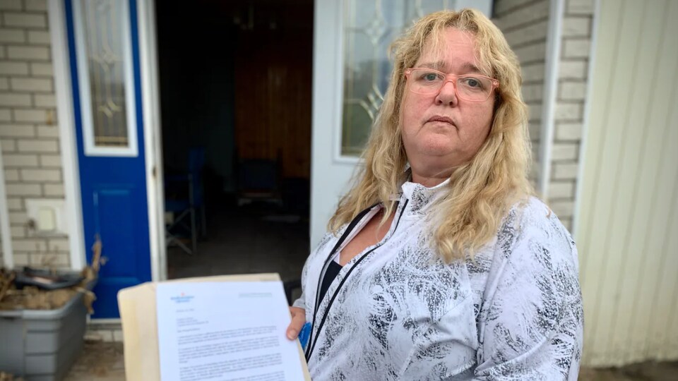Mme Anderson, debout devant sa maison, tient le document dans ses mains.