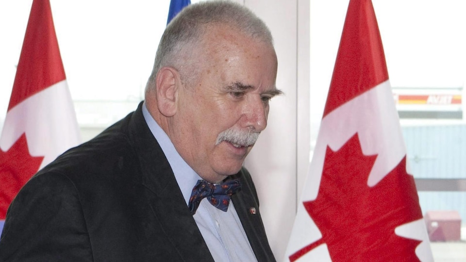 Photo d'André Arthur en costume devant deux drapeaux du Canada.