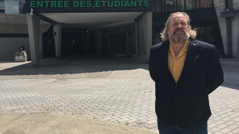 A man poses in front of a college building. 