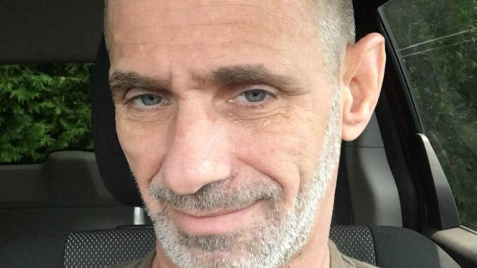 On voit le visage de l'homme, qui est assis dans sa voiture, en gros plan.
