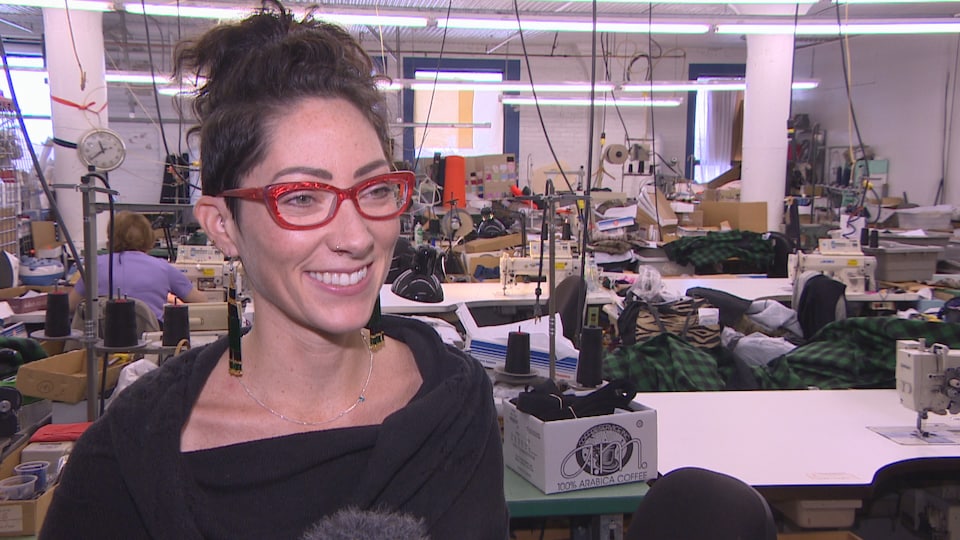 Andréanne Dandeneau est dans son atelier de vêtements, Il y a des machines à coudre, des boîtes et des tissus.