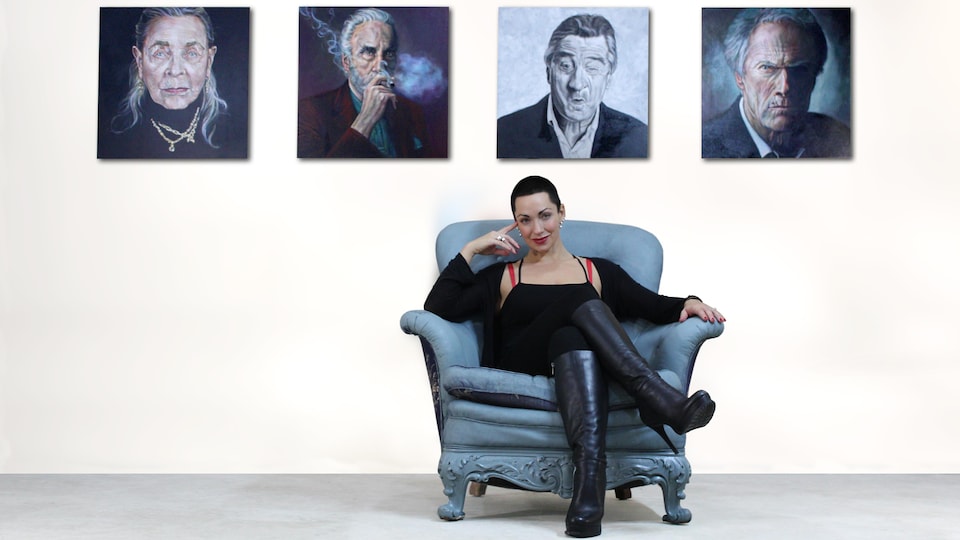 Angela Hardy assise devant quelques-unes de ses oeuvres.