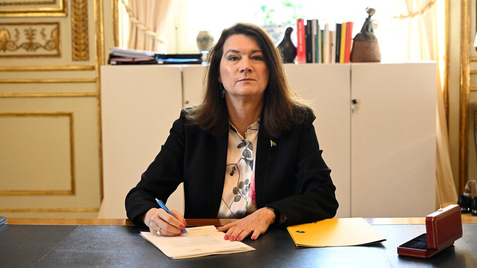 Ann Linde, holding pencil, at her desk. 