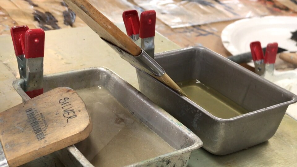 Deux bacs contiennent de la peinture à l'encaustique. Un pinceau est placé dans la cire fondue.