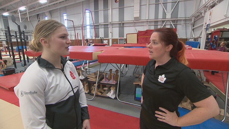 Anne-Jolie Roy et son entraîneuse Rachel Drouin Germain discutent devant un trampoline.