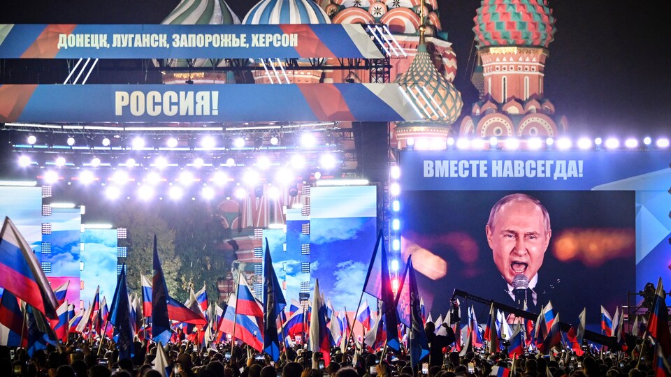 Vladimir Poutine est projeté sur un écran géant, devant une foule, sur la place Rouge, en Russie.