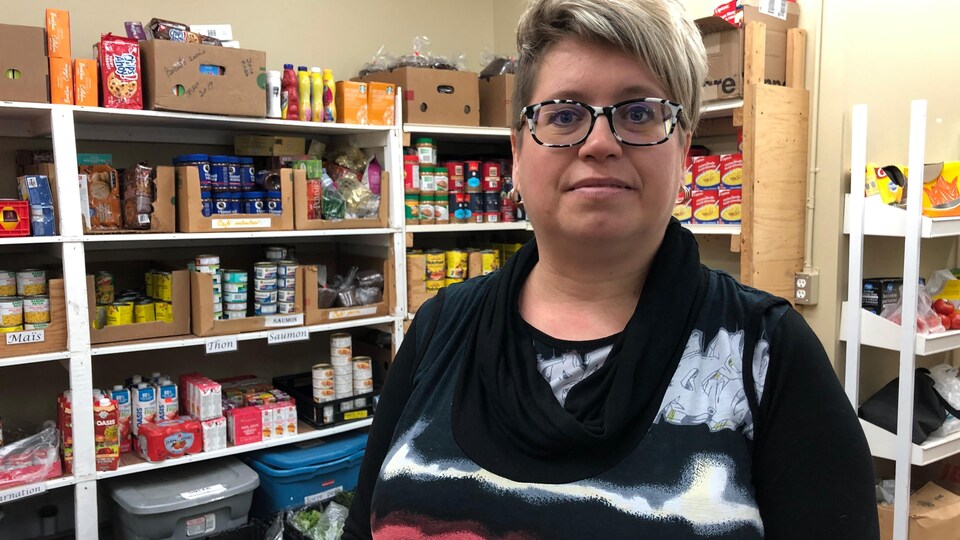 Une femme se tient debout devant des étagères contenant des denrées non périssables. 