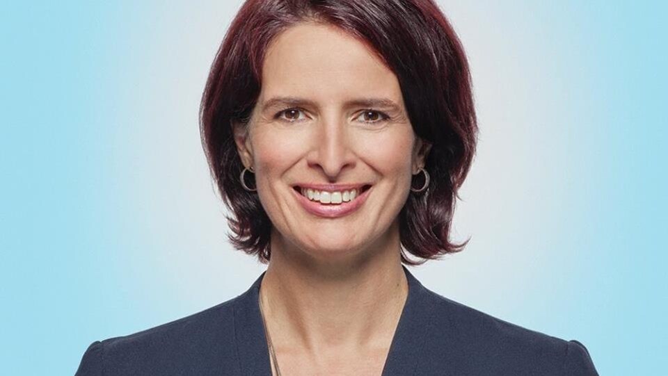 Une femme dans la quarantaine. Un plan rapproché, elle regarde la caméra. Elle a les cheveux courts bruns. Elle porte un veston bleu.