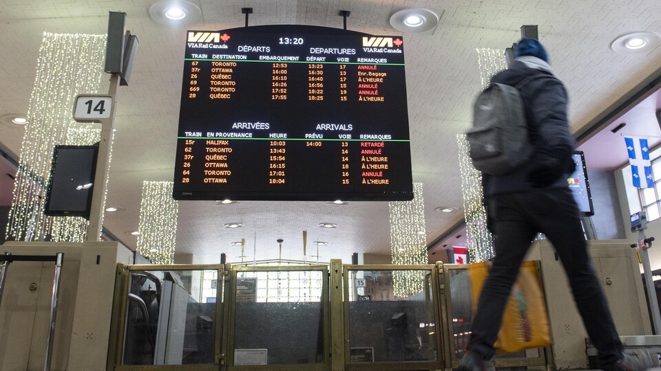Une personne marche devant un panneau annonçant les horaires des trains à la gare Centrale de Montréal.