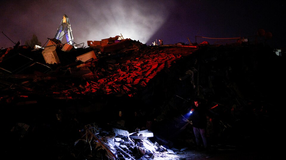 Un homme utilise une lampe de poche à la recherche de survivants sous les décombres en pleine nuit.
