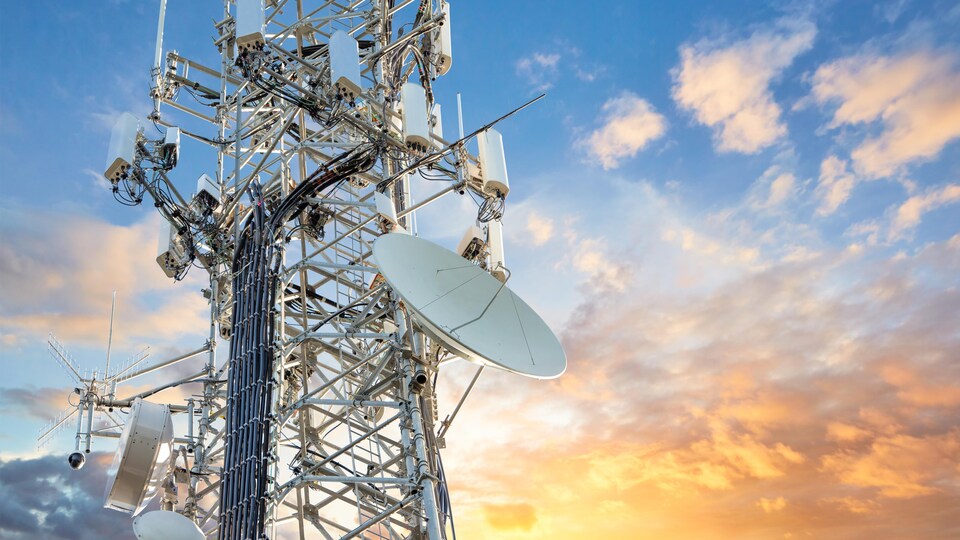 Une tour de transmission 5G devant un coucher de soleil.