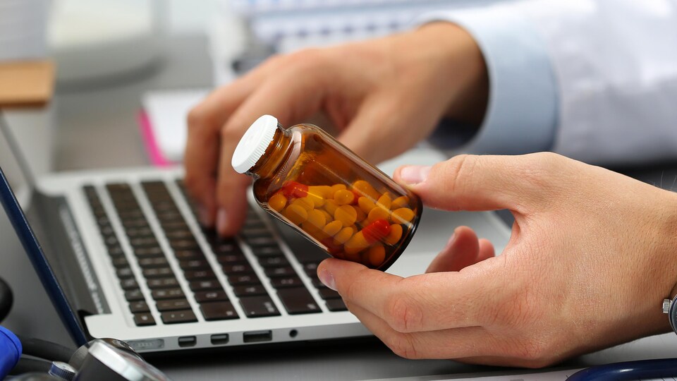 Un médecin tient un flacon de médicaments et tape sur un ordinateur portable.
