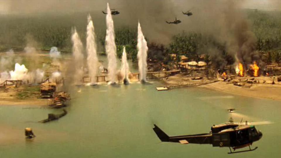 Des hélicoptères survolent un lac. On voit aussi des colonnes d'eau soulevées par des bombes, des feux et de la fumée sur le paysage.