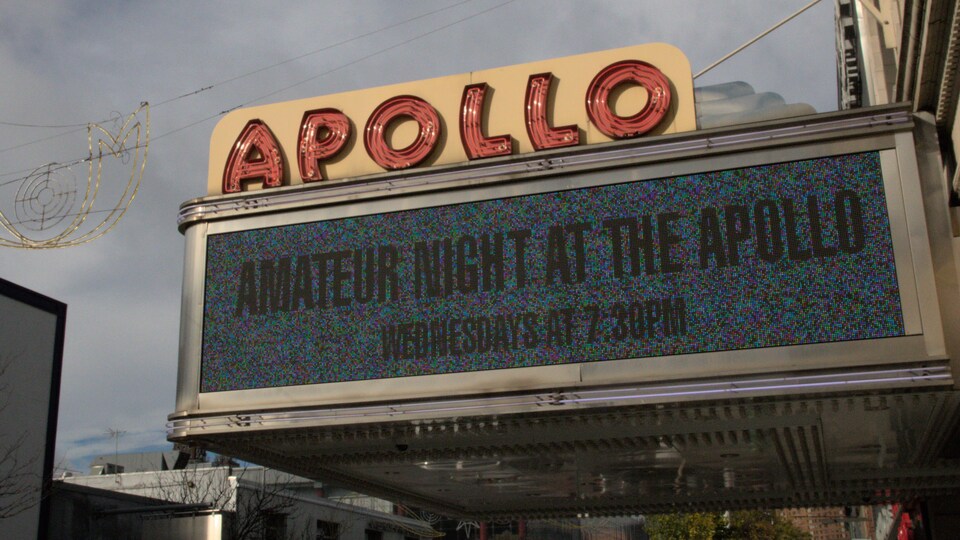 Une devanture de salle de spectacle, avec une enseigne lumineuse indiquant Apollo. Dessous, il est possible de lire Amateur Night at The Apollo. 