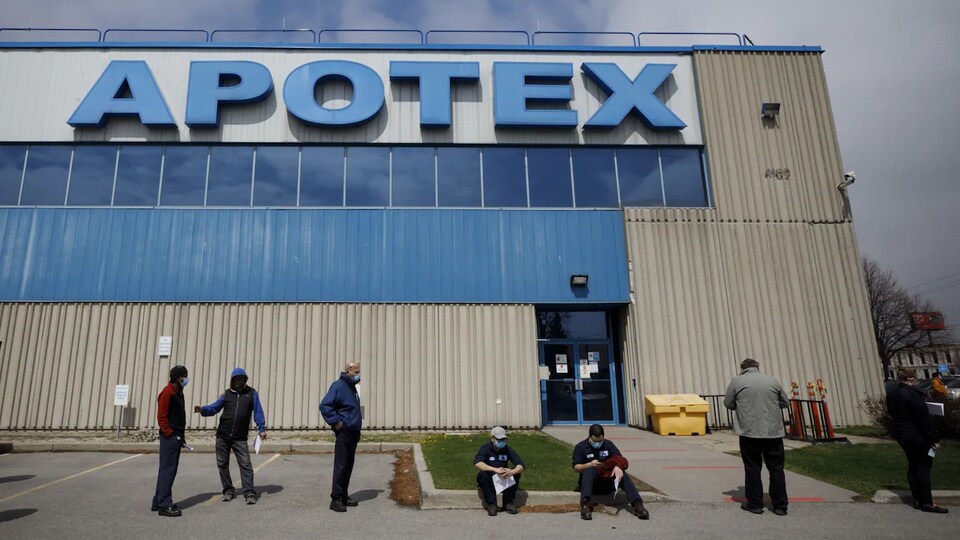 Des travailleurs qui portent un masque font la file à l'entrée de l'usine torontoise d'Apotex.