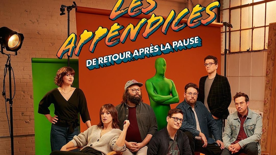 Quatre hommes et deux femmes posent à côté d'une personne habillée d'une combinaison verte de la tête aux pieds.