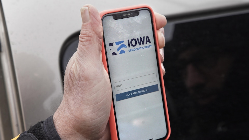 Un homme tient dans sa main son téléphone cellulaire; on y voit l'application Iowa Democratic Party.