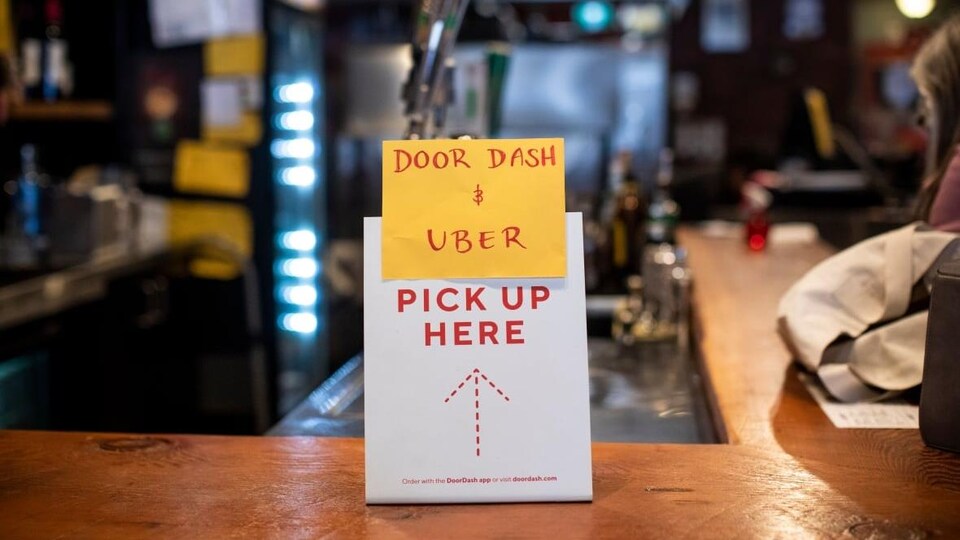 Un comptoir de restaurant, sur lequel un petit écriteau indique que les employés de Uber et Door Dash doivent prendre les commandes ici.