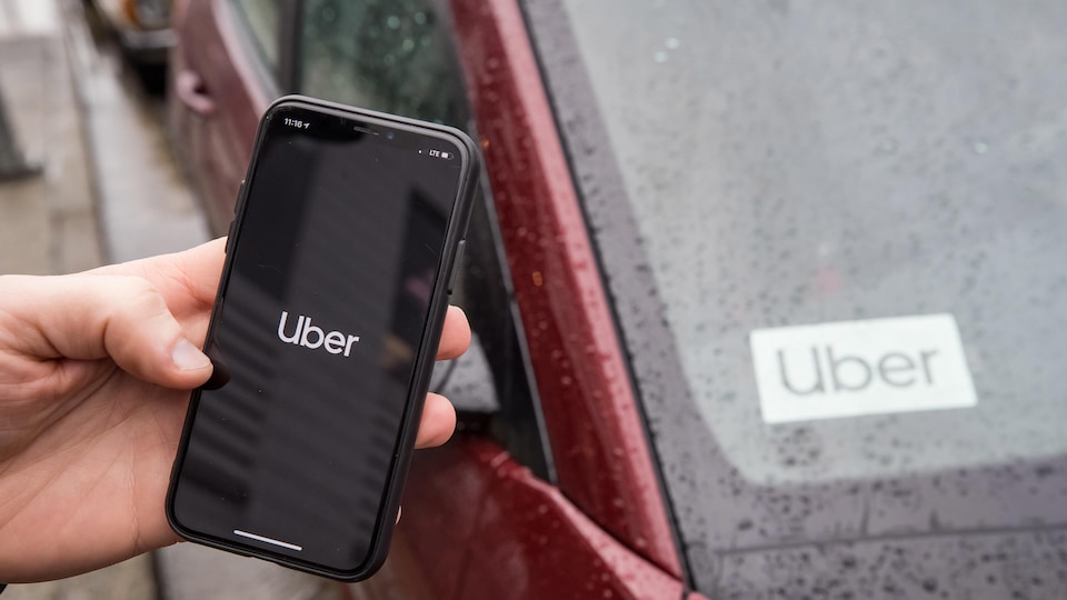Une main tient un téléphone sur lequel est écrit le mot Uber. 