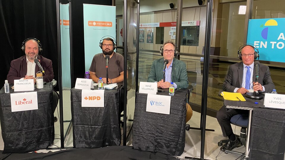 Les candidats assis à des tables individuelles séparées par un plexiglas.