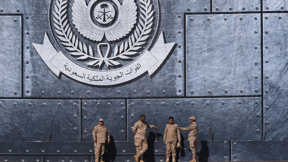 Des officiers de l'armée saoudienne discutent dans la capitale, Riyad. Derrière eux, on peut voir un logo des forces nationales de l'Arabie saoudite.