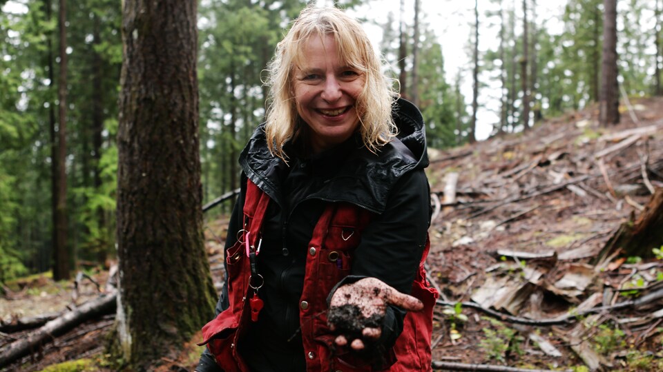 Suzanne Simard, dans une forêt, tenant de la terre dans sa main