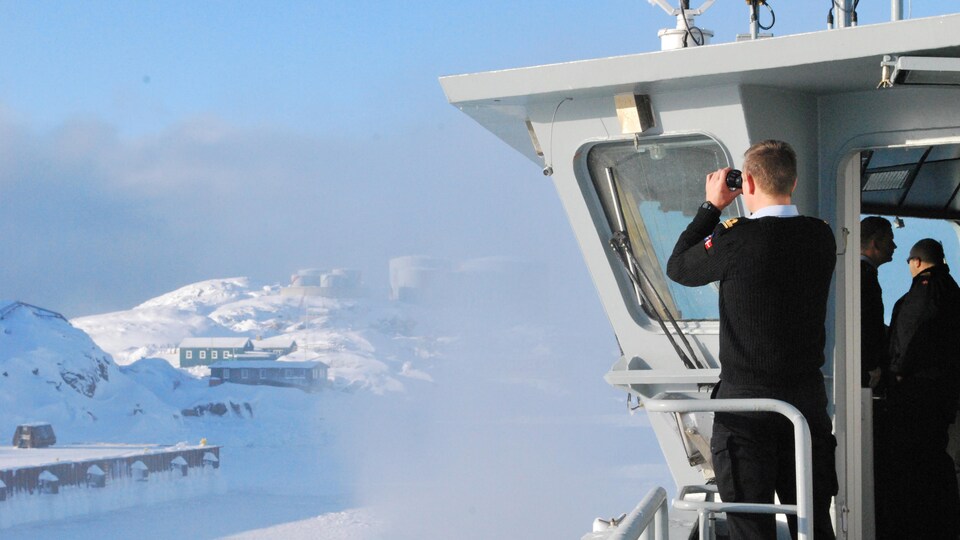 Un membre d'un navire d'inspection danois observe avec des jumelles au loin.