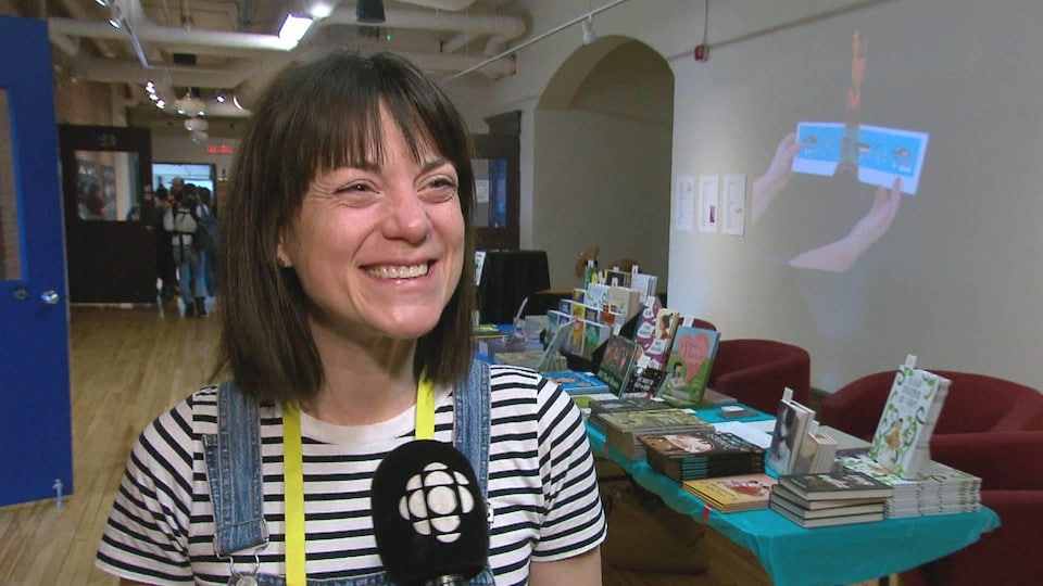 Une femme debout près d'un étalage de livres fait un grand sourire.