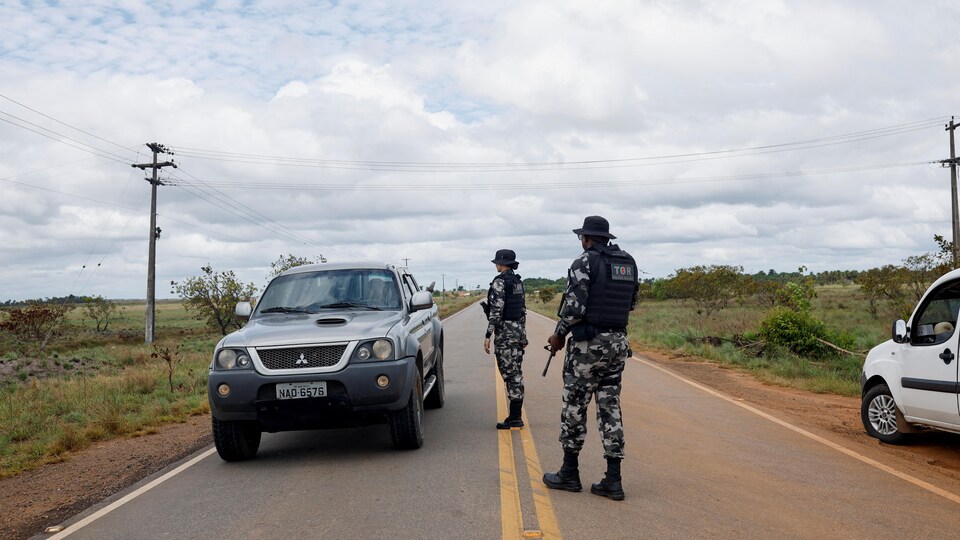 Deux membres des forces armées arrêtent un véhicule sur une route. 