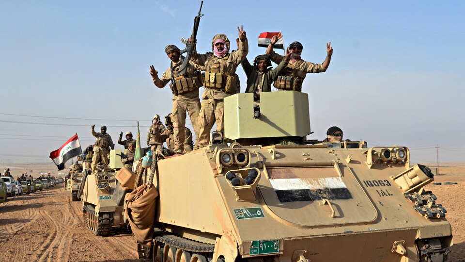Des soldats irakiens, sur des tanks, font le V de la victoire.