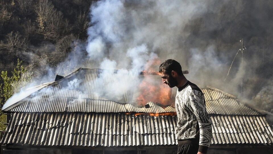 Un homme passe devant une maison en feu.