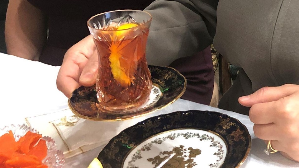 Une main tient un verre de thé placé sur une sous-tasse.