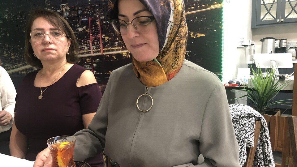 Nazola Isjandorova et une autre femme sont assises côte à côte à une table. Nazola tient le verre armudu rempli de thé.