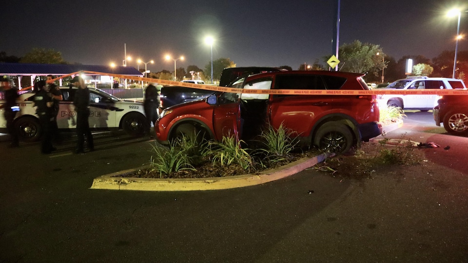 Une voiture accidentée, des policiers et des rubans dans un stationnement la nuit.