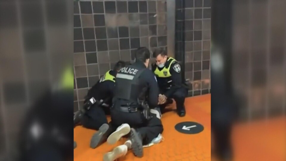 Une image prise avec un cellulaire où l'on voit un policier et deux inspecteurs accroupis, et les pieds d'une personne qui dépassent sous le policier.