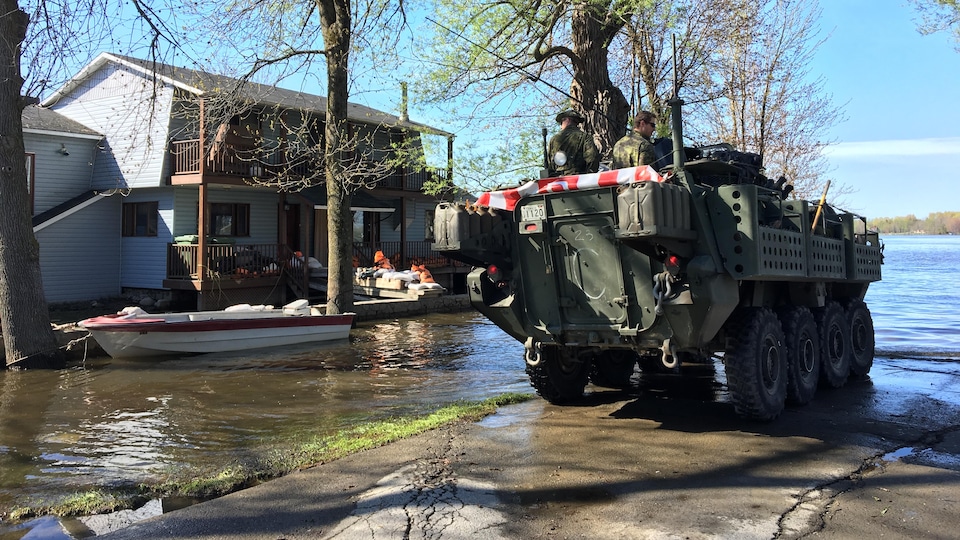 Arrivée d'un groupe de militaires des Forces armées canadiennes dans le secteur inondé de la rue Fournier, à Saint-André-d'Argenteuil; on voit une maison et un bateau en arrière-plan.