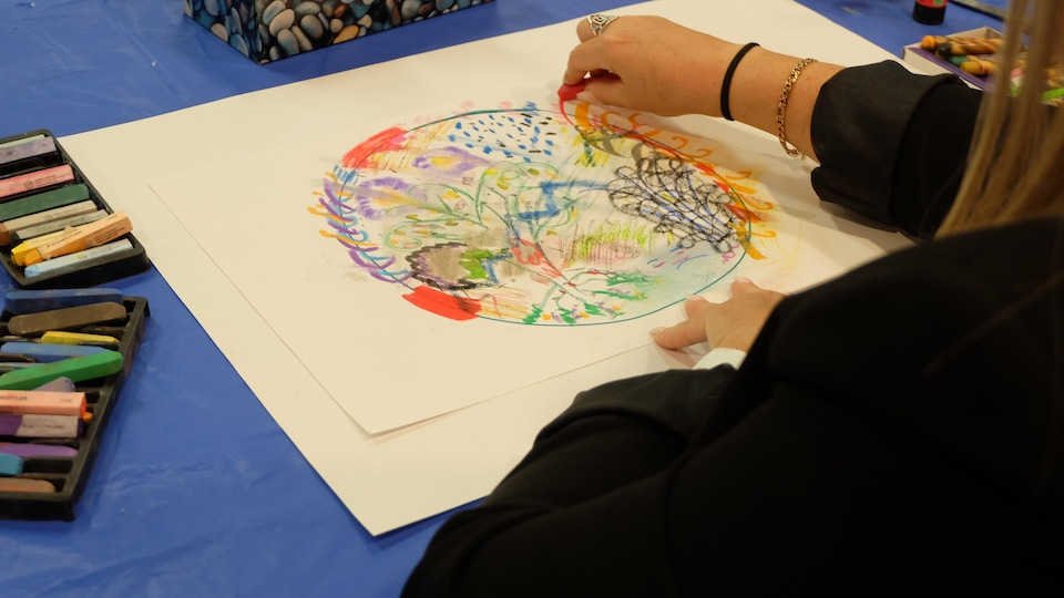 Une femme de dos qui dessine dans un cercle. Ce sont surtout des traits de pastels de couleur. 