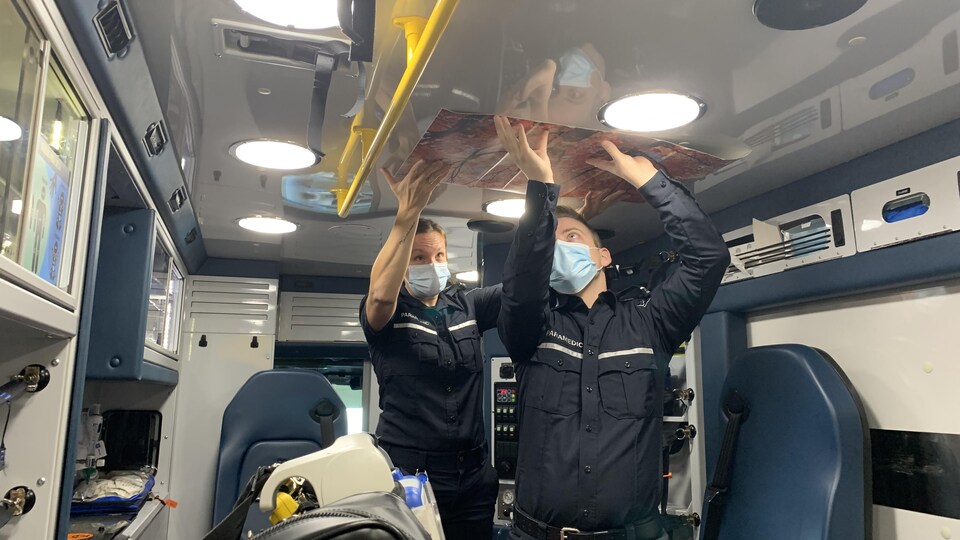 Deux ambulanciers collent une oeuvre d'art au plafond de l'ambulance.