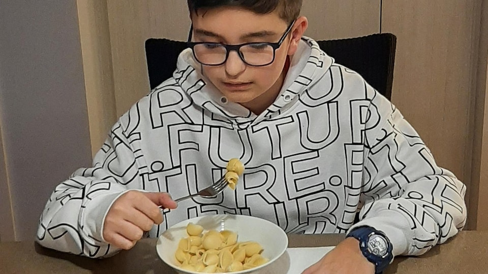 Un adolescent mange un bol de pâtes à table.
