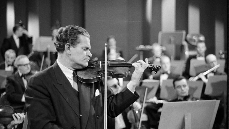Violoniste qui joue les yeux fermés et orchestre en arrière plan.