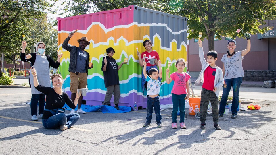 Des adultes et des enfants, pinceaux en main, devant un conteneur multicolore.