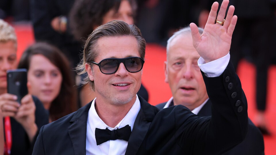 Brad Pitt sourit et fait un signe de la main sur un tapis rouge.