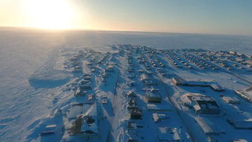 La communauté d'Arviat sous la neige photographiée de haut en avril par un drone avec le soleil à l'horizon.